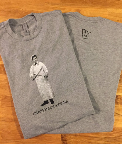 Gray cotton Frank-on-T t-shirt inspired by Grandpa Frank Boerboon, a former butcher for JJ Hill. The front center image shows a man sharpening knifes with Craftmade Aprons underneath. Designed and produced by Craftmade Aprons, Minnesota.