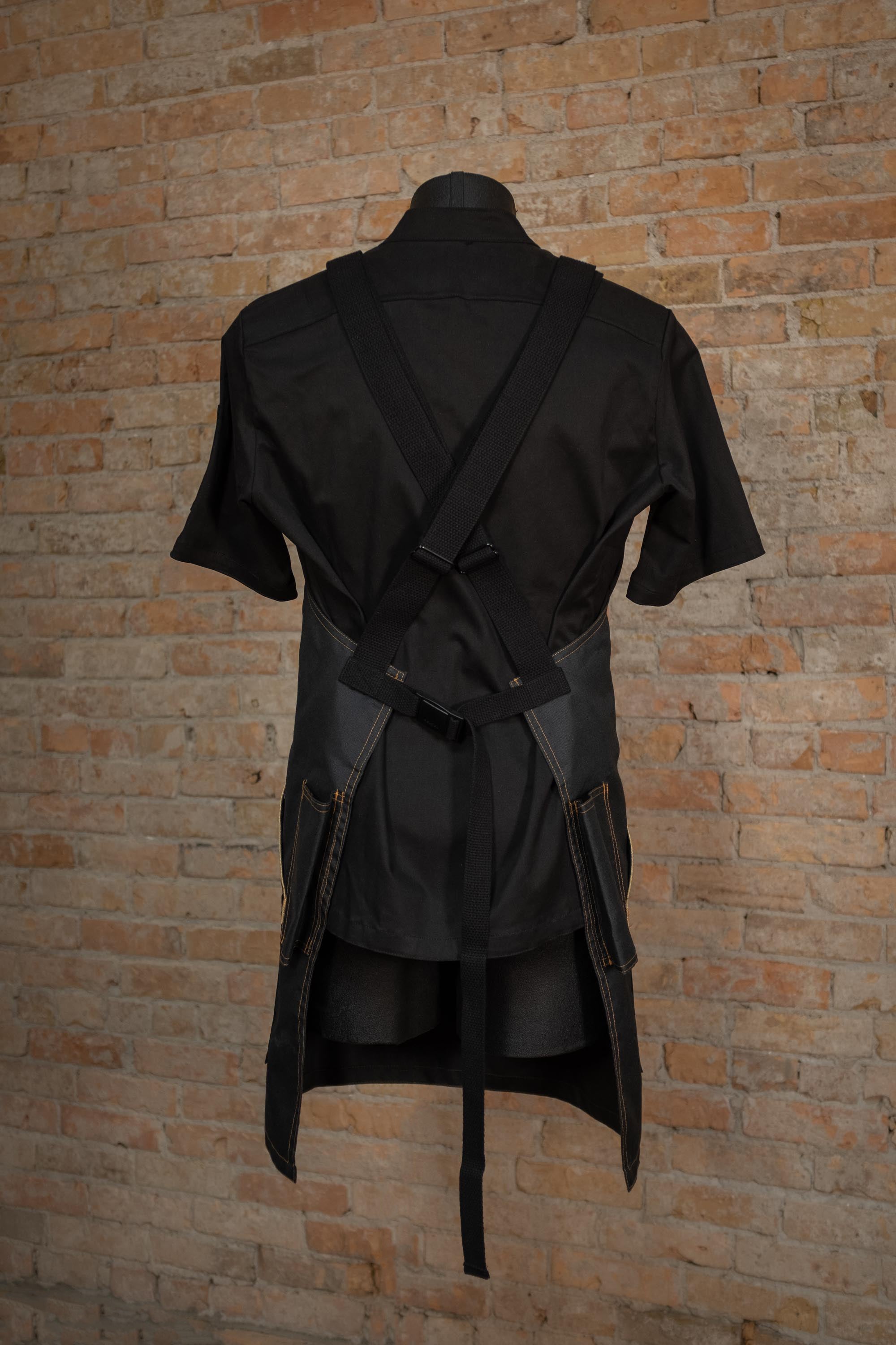 Protective Kevlar cross back apron from Craftmade Aprons, Minnesota, displayed on a mannequin over a black chef coat. The BAMF apron is shown from the back, displaying the black cross back strapping.