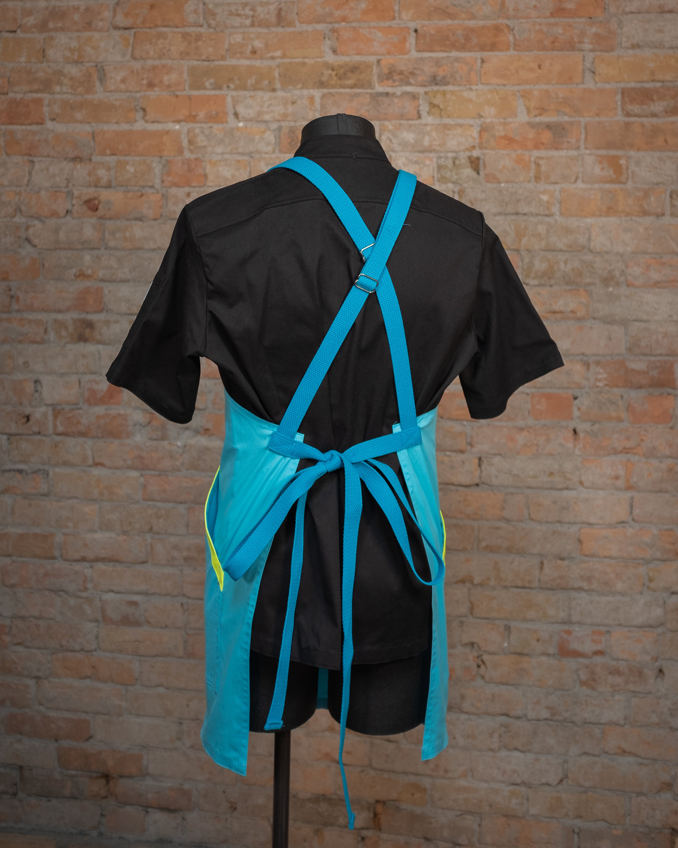 Italian cotton crossback apron from Craftmade Aprons, Minnesota, displayed on a mannequin over a black chef coat. The apron 'Billy Ocean' is shown from the back, showing off the ocean blue crossback strapping.