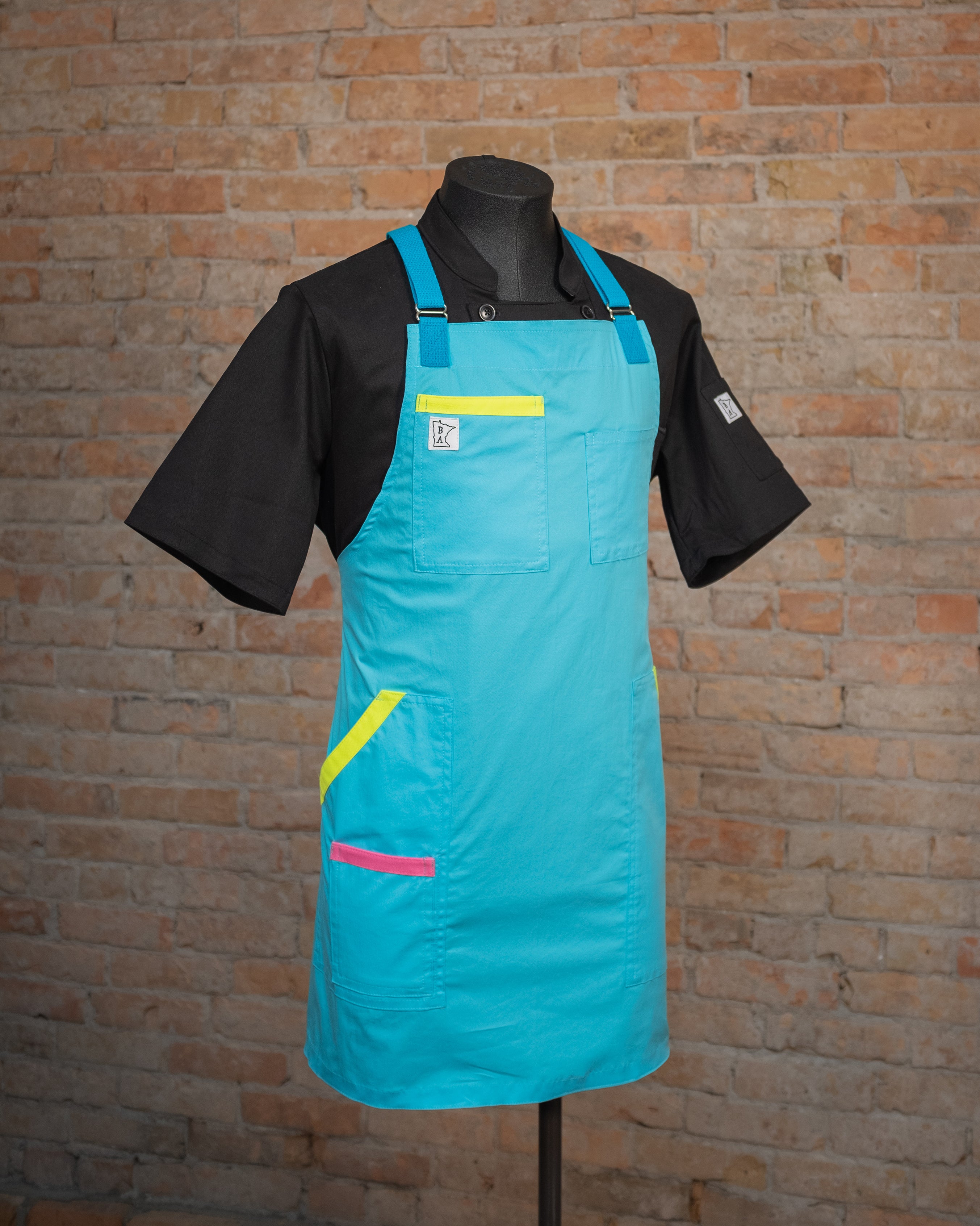 The Italian cotton design 'Billy Ocean', displayed on a mannequin over a black  chef coat. Both the coat and apron were designed and produced by Craftmade Aprons in Minnesota.