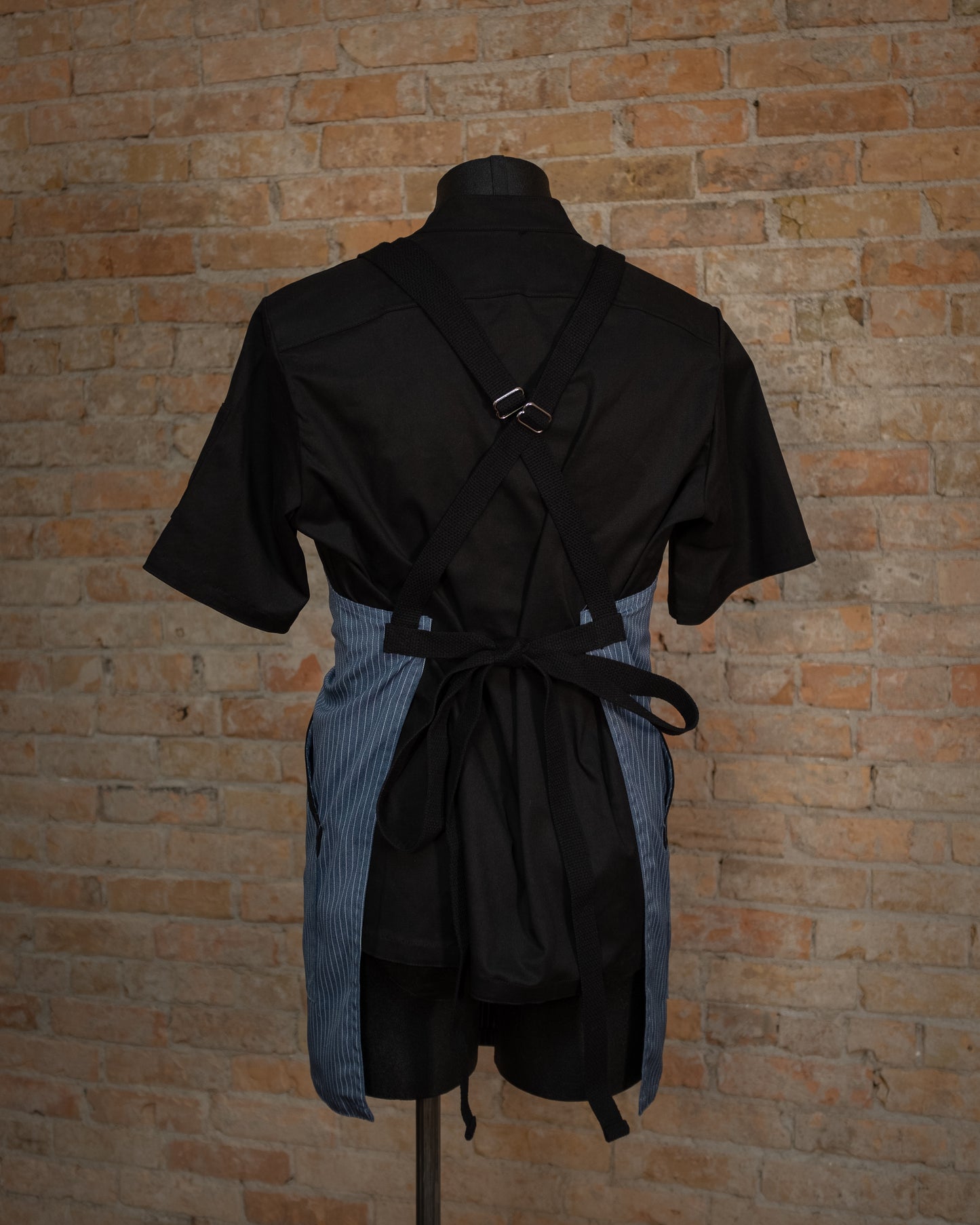 Poly/cotton twill crossback apron from Craftmade Aprons, Minnesota, displayed on a mannequin over a black chef coat. The apron Culinary Gangster is shown from the back, displaying the black crossback strapping.