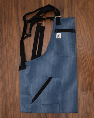 Poly/cotton twill fabric blue pinstriped apron with the complementary pockets and black strapping. The apron design Culinary Gangster was manufactured in Minnesota by Craftmade Aprons. Comes in two other base colors of black or gray.