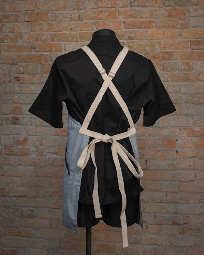 Lightweight cotton/poly crossback apron from Craftmade Aprons, Minnesota, displayed on a mannequin over a black chef coat. The apron Cloudy With a Chance is shown from the back, displaying the natural colored crossback strapping.