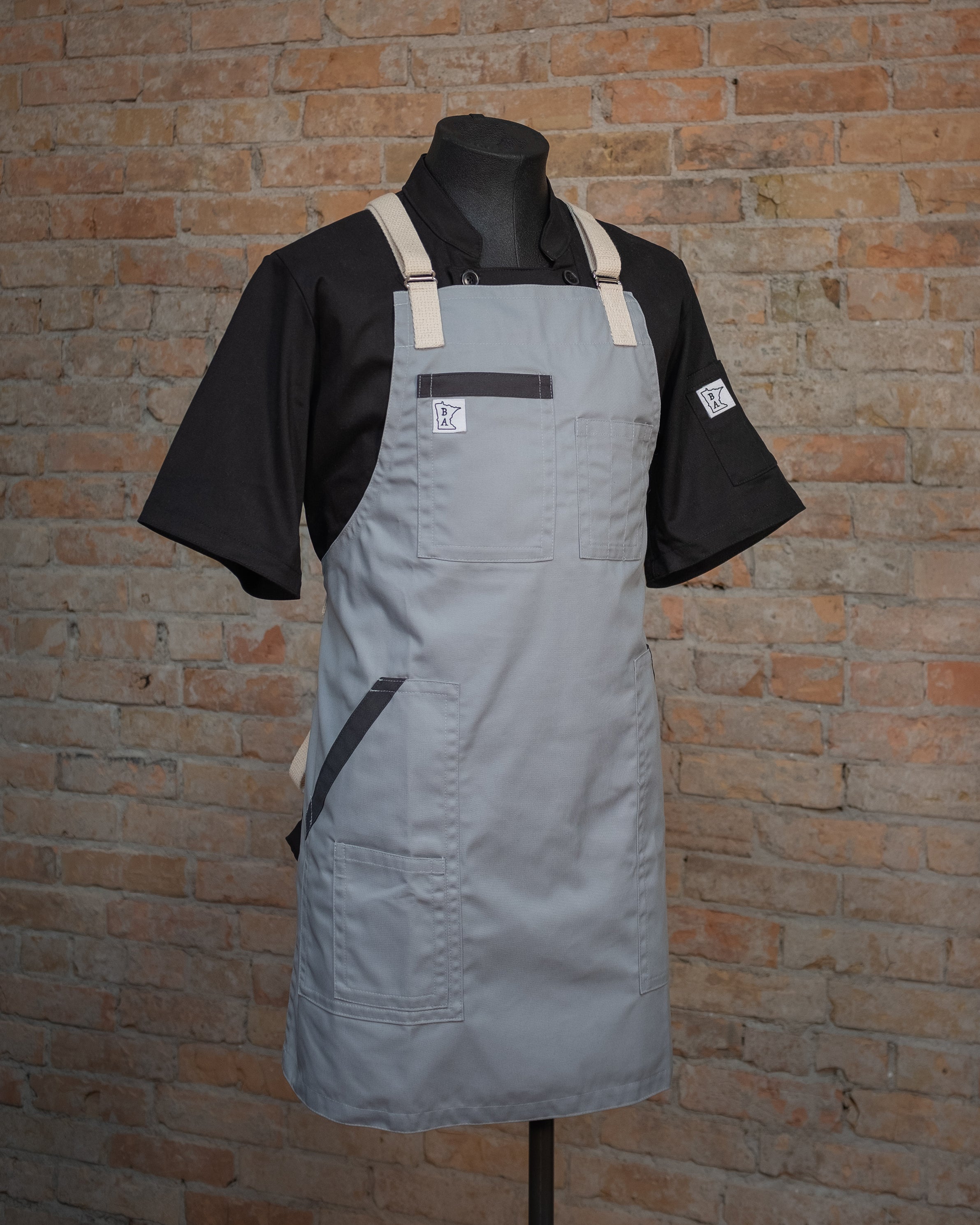 The lightweight cotton/poly apron design Cloudy With a Chance displayed on a mannequin over a black chef coat. Both the chef coat and the apron were designed and produced by Craftmade Aprons, Minnesota.