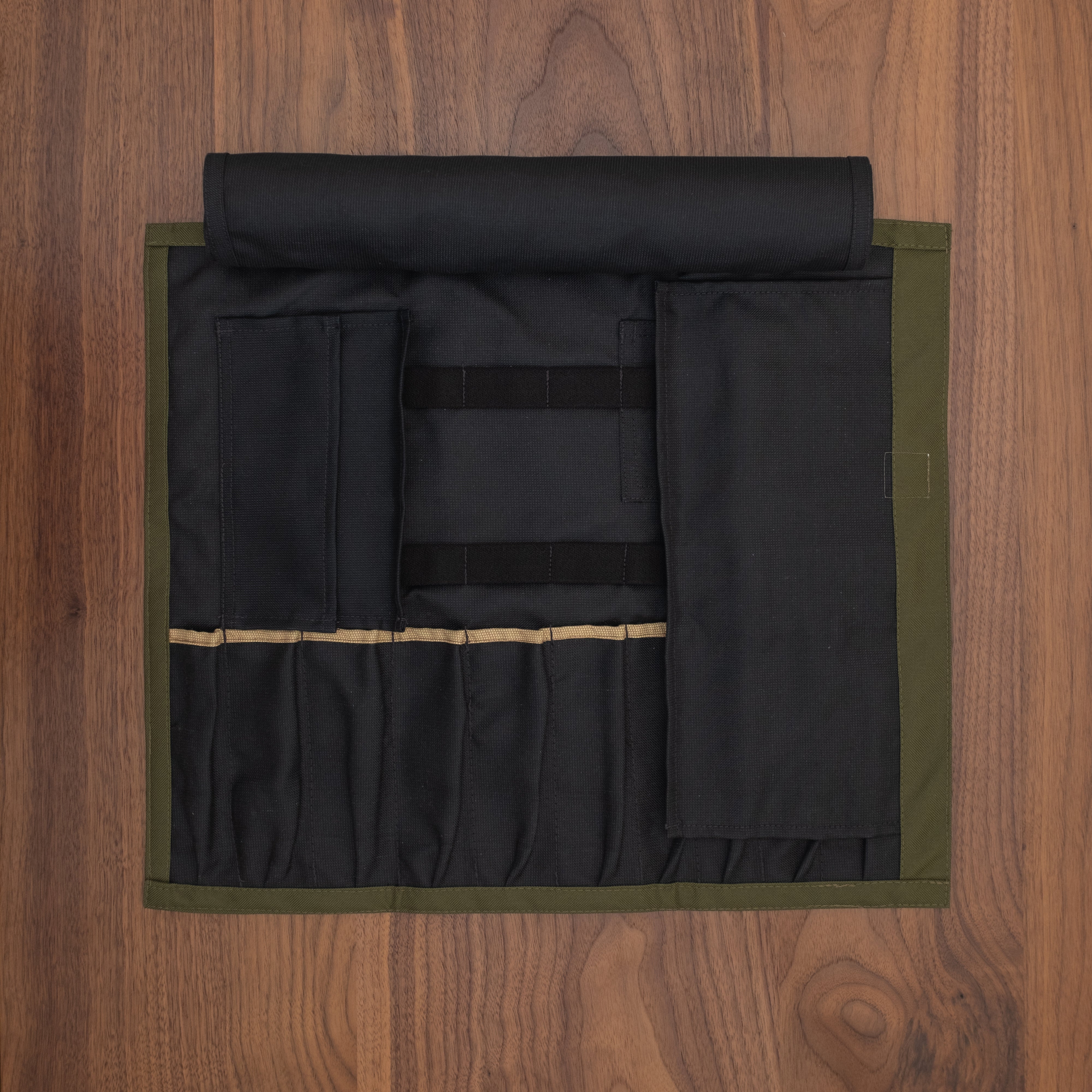 Black interior of the Ottertex Edition Olive/Orange Side Hustle knife roll laid out flat on a wooden surface. The interior is made of a 50-50 Kevlar/Nomex blend for long lasting protection. Design by Craftmade Aprons in Minnesota.