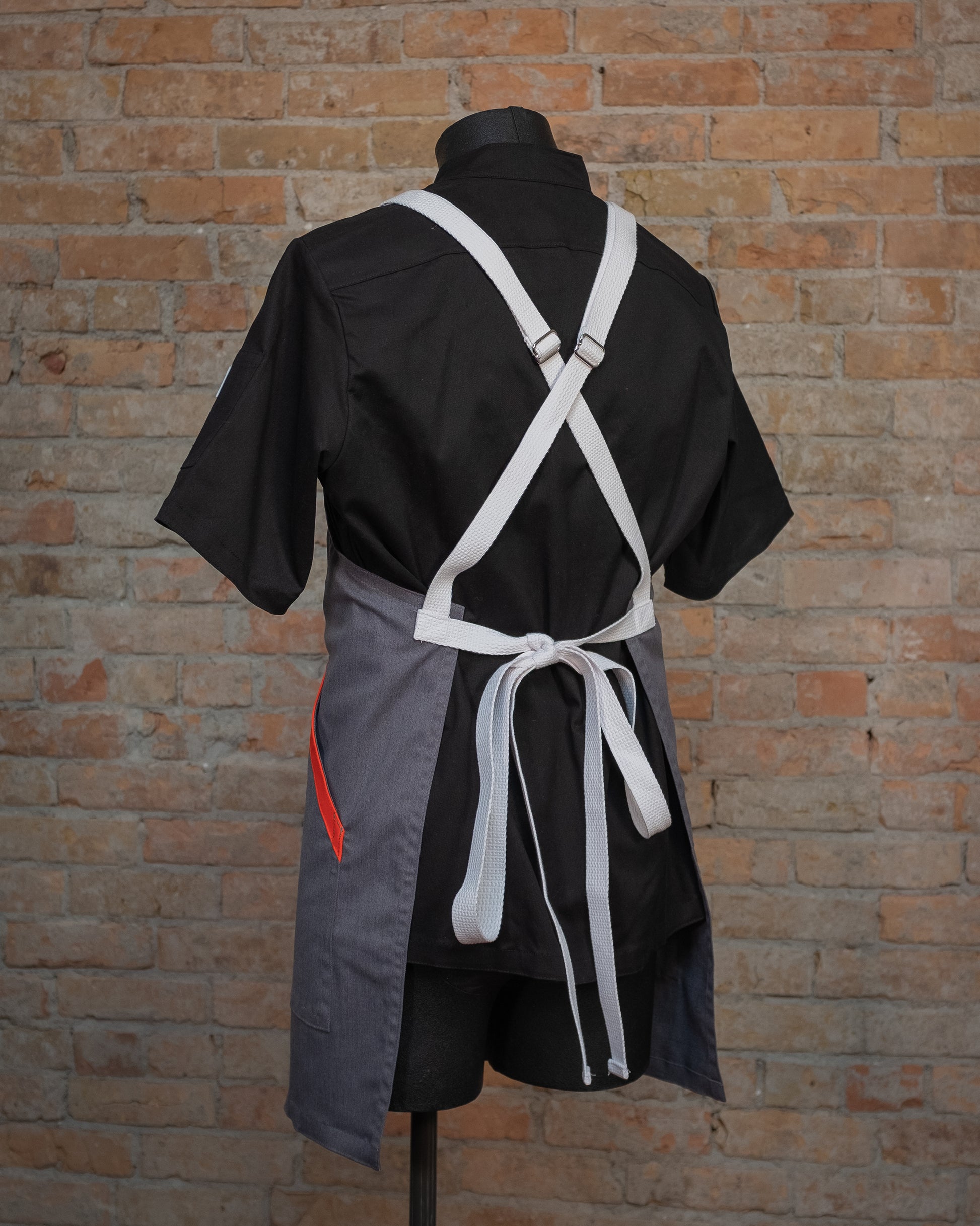 Cotton crossback apron from Craftmade Aprons, Minnesota, displayed on a mannequin over a black chef coat. The apron Dreamsicle is shown from the back, accentuating the bright white crossback strapping. 