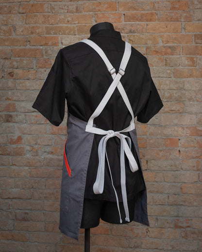 Cotton crossback apron from Craftmade Aprons, Minnesota, displayed on a mannequin over a black chef coat. The apron Dreamsicle is shown from the back, accentuating the bright white crossback strapping. 