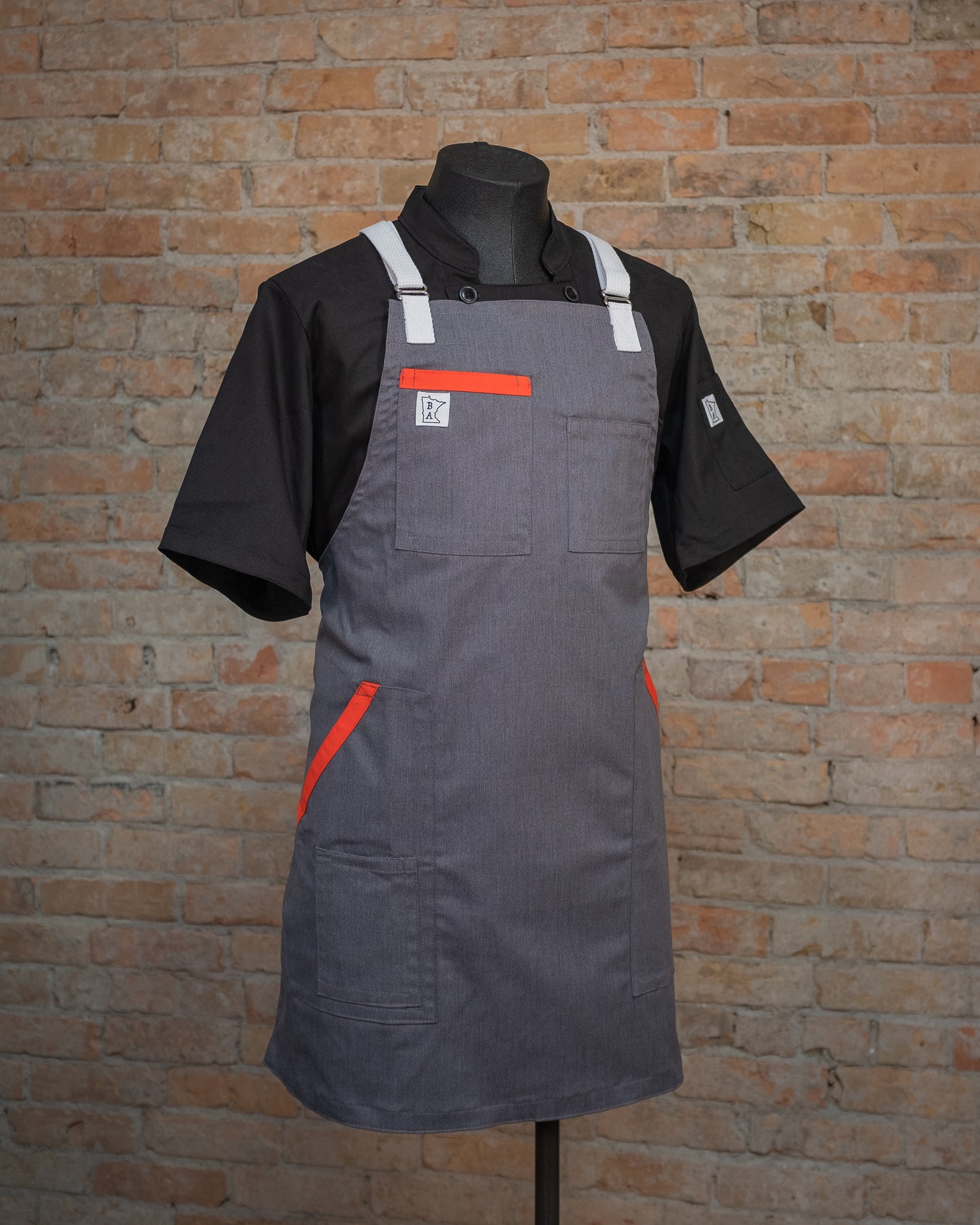 The cotton apron design Dreamsicle displayed on a mannequin over a black chef coat. Both the chef coat and apron were designed and produced by Craftmade Aprons, Minnesota. 