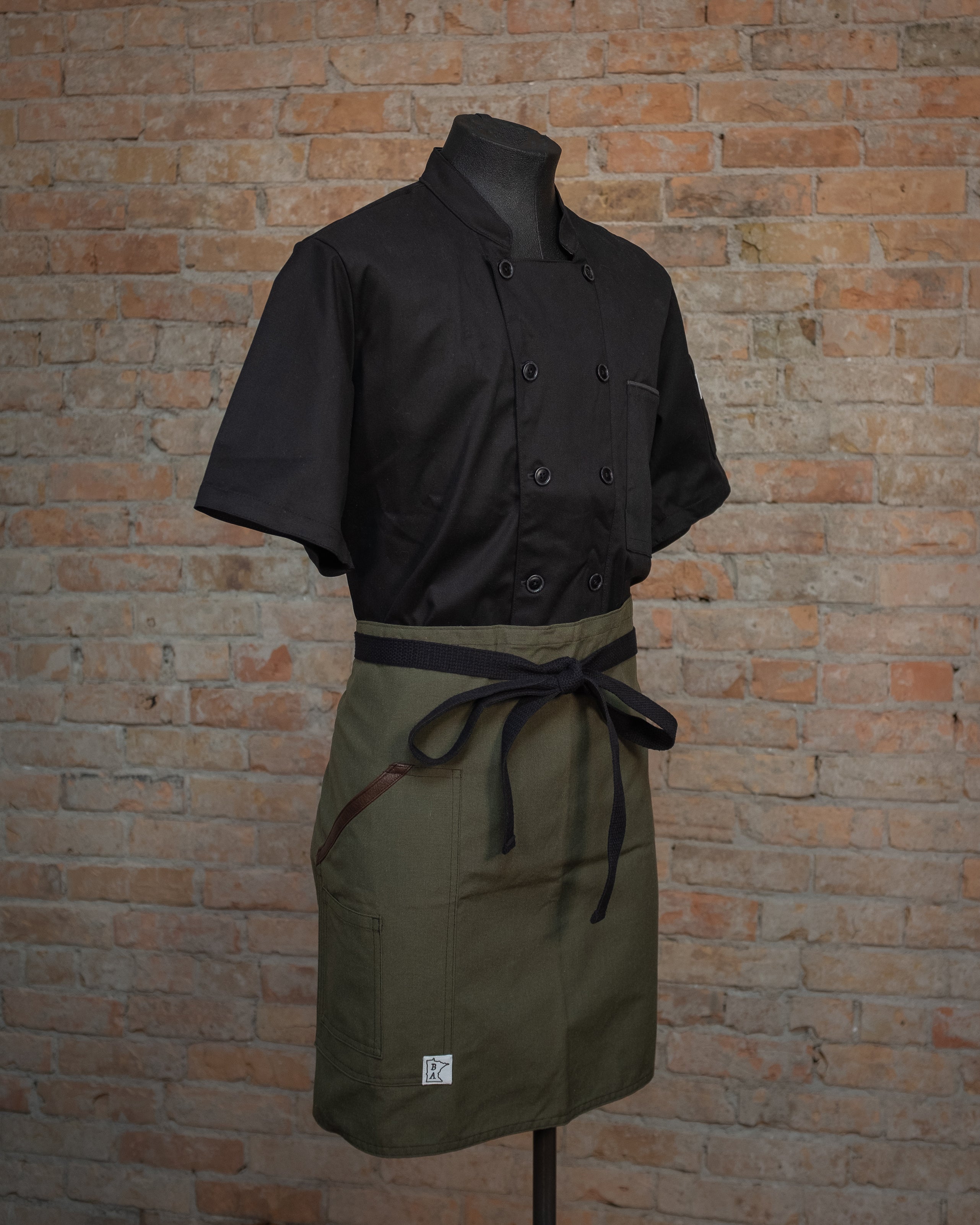 The Nomex-Kevlar apron design Fire Watch displayed on a mannequin's waist over a black chef coat. Both the chef coat and the apron were designed and produced by Craftmade Aprons, Minnesota. 