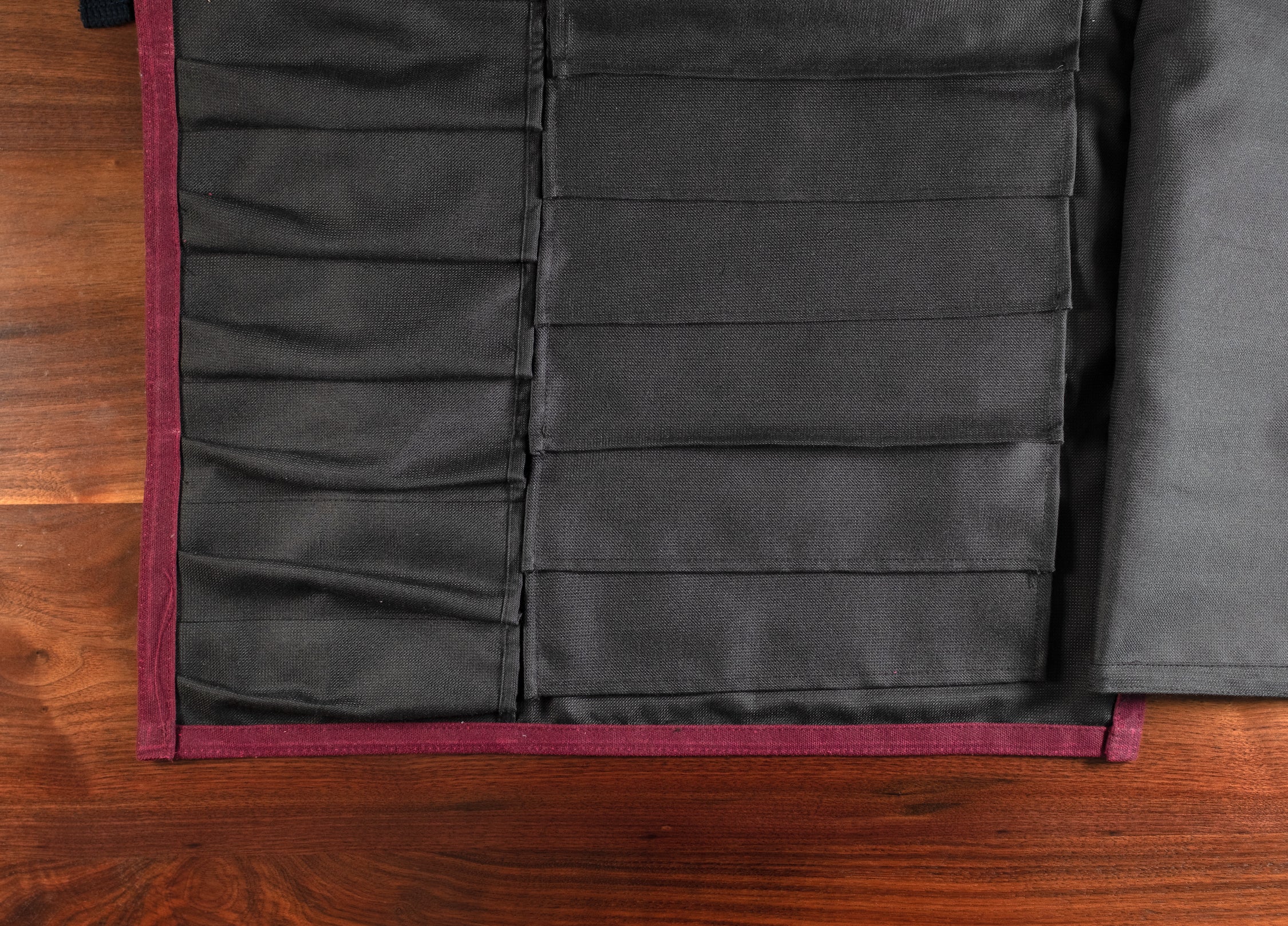 Product shot of the interior of the Main Squeeze burgundy knife roll displaying all of the knife and utensil pockets. Designed by Craftmade Aprons, Minnesota.