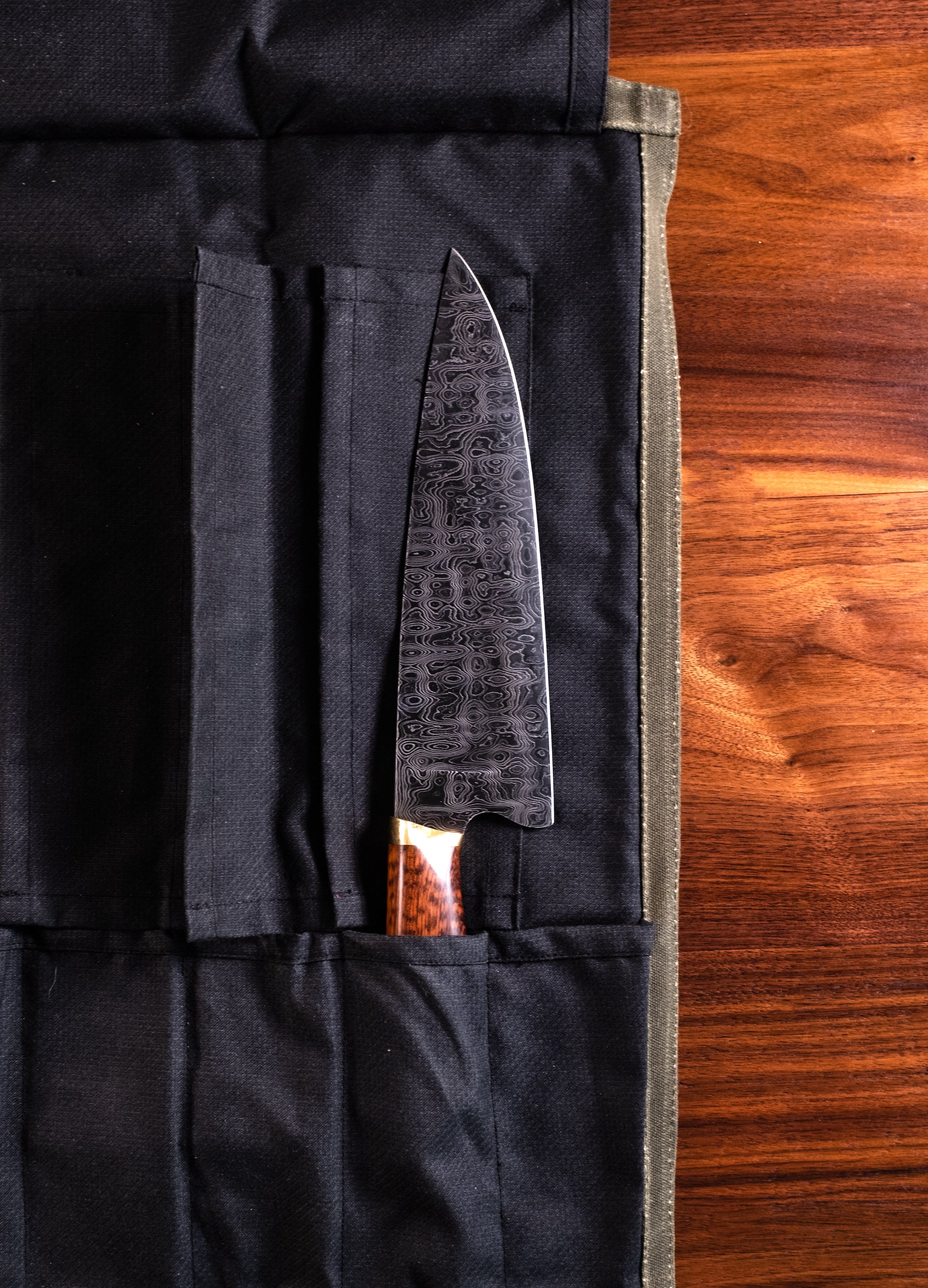 Product shot of a knife tucked into a pocket in the interior of the Main Squeeze olive green knife roll. Handcrafted in Minnesota by Craftmade Aprons. 