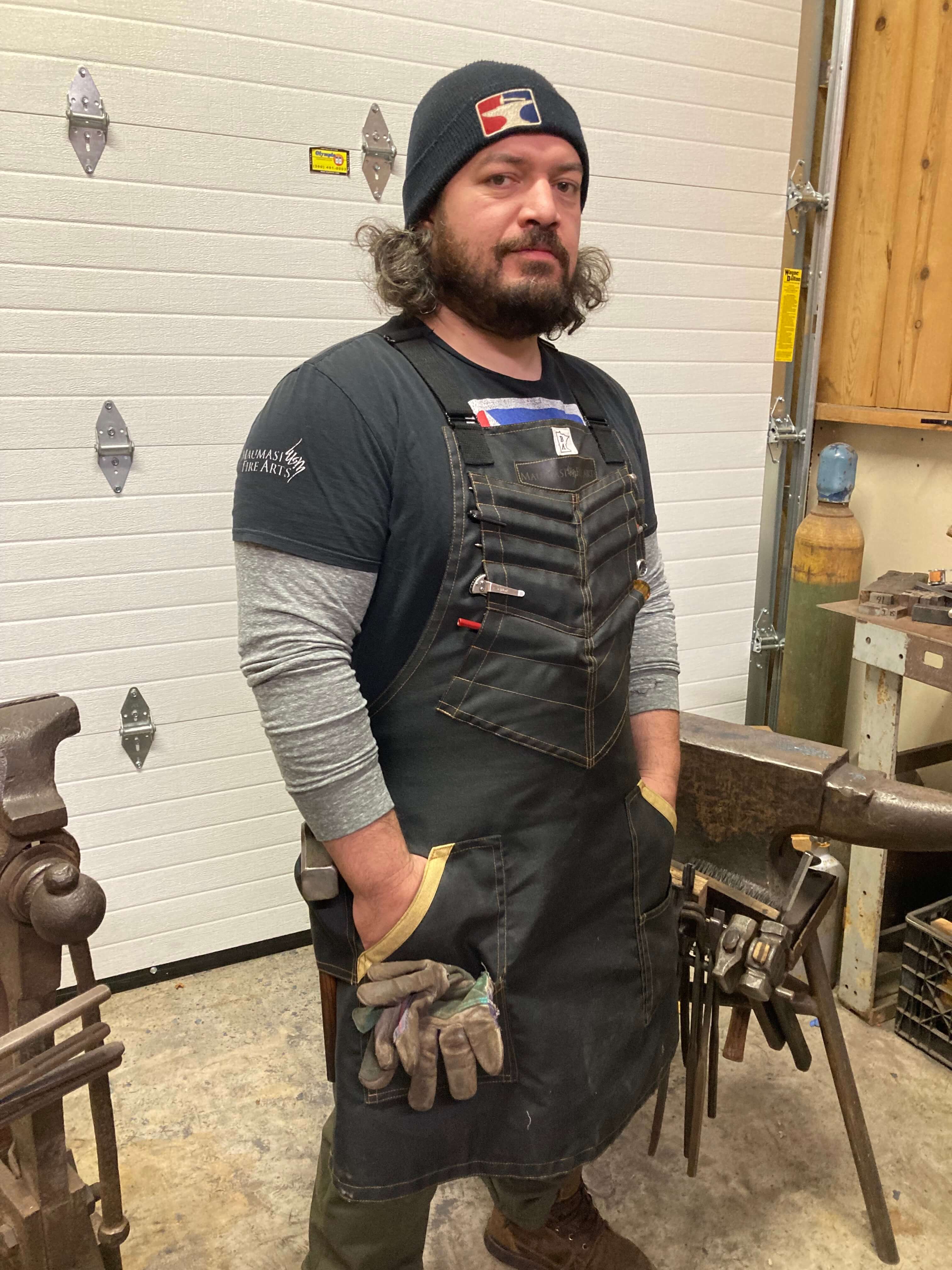 Image of Mareko Maumasi wearing the BAMF apron. The BAMF is a heavy-duty, protective Kevlar apron in black with yellow threading, and the perfect protective apron for knife makers. 