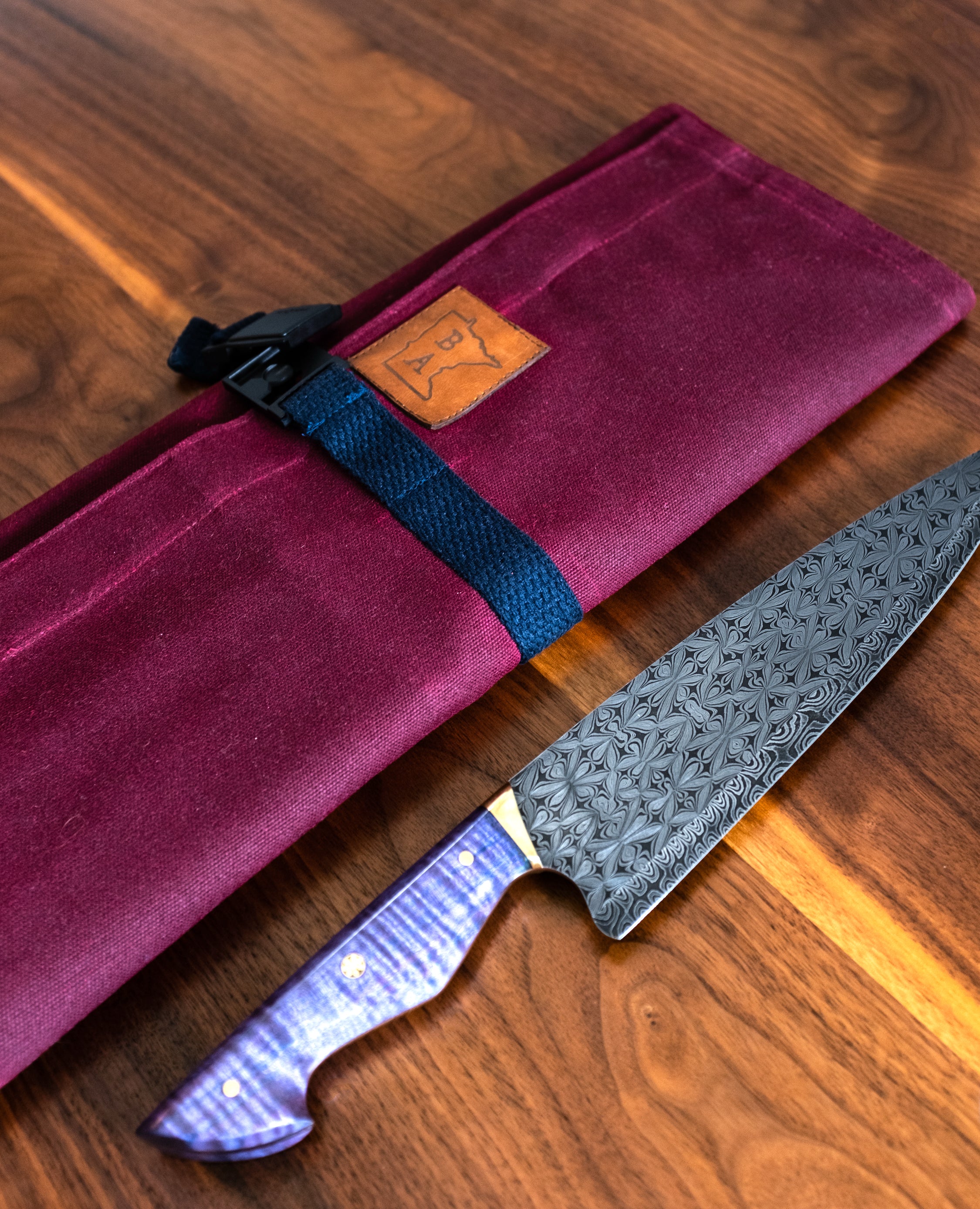 Angled product shot of a knife lying next to Side Hustle -Burgundy- knife roll. From Craftmade Aprons, based in Minnesota.