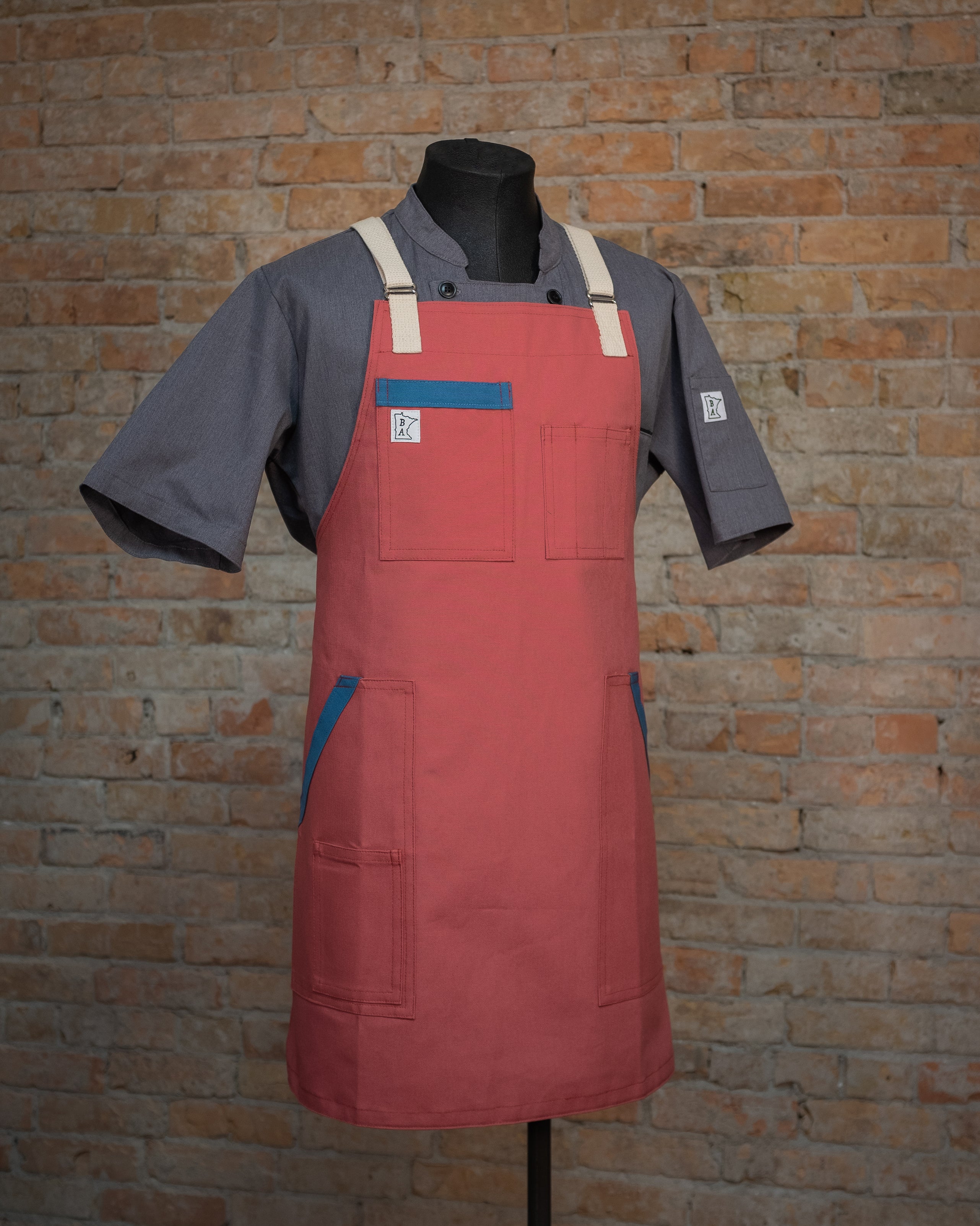 The duck cloth apron design Sockeye displayed on a mannequin over a gray chef coat. Both the chef coat and the apron were designed  and produced by Craftmade Aprons, Minnesota.