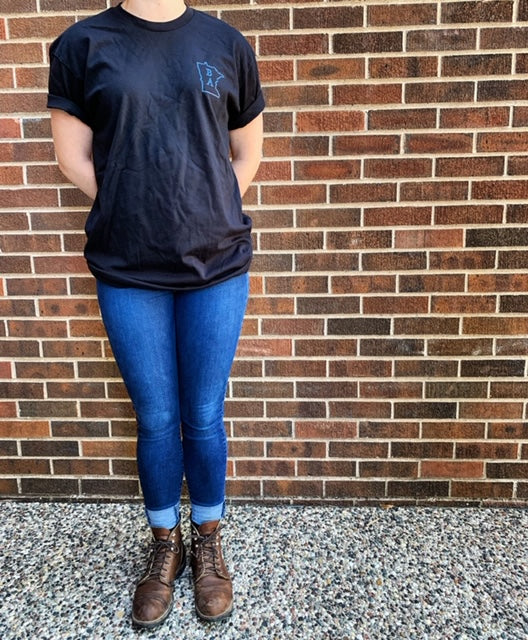 A model wearing the Black and Blue T-shirt with jeans and brown boots. T-shirt designed and sold by Craftmade Aprons, Minnesota.