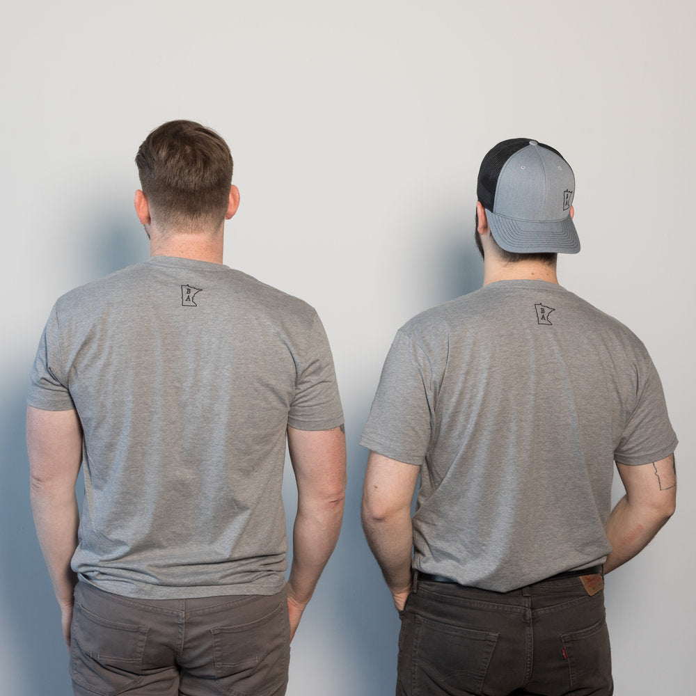 Two men against a white wall wearing the Frank-on-T t-shirt. This gray cotton t-shirt has a small BA logo in between the shoulder blades of the shirt. One man is also wearing the gray BA cap. The cap and the t-shirt were manufactured in Minnesota by Craftmade Aprons.