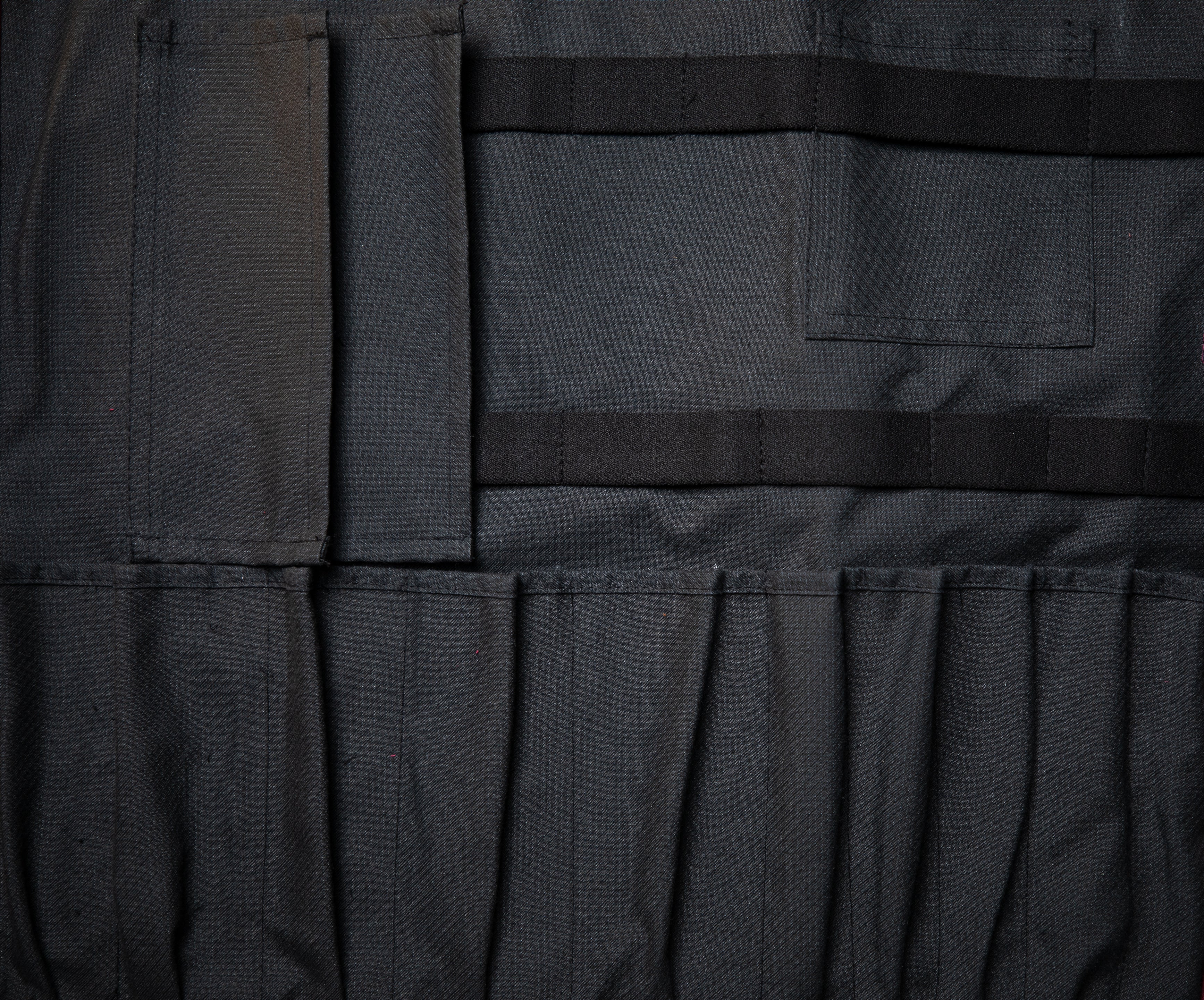 Black interior of the Side Hustle olive knife roll laid out flat on a wooden surface. The interior is made of a 50-50 Kevlar/Nomex blend for long lasting protection. Design by Craftmade Aprons in Minnesota.
