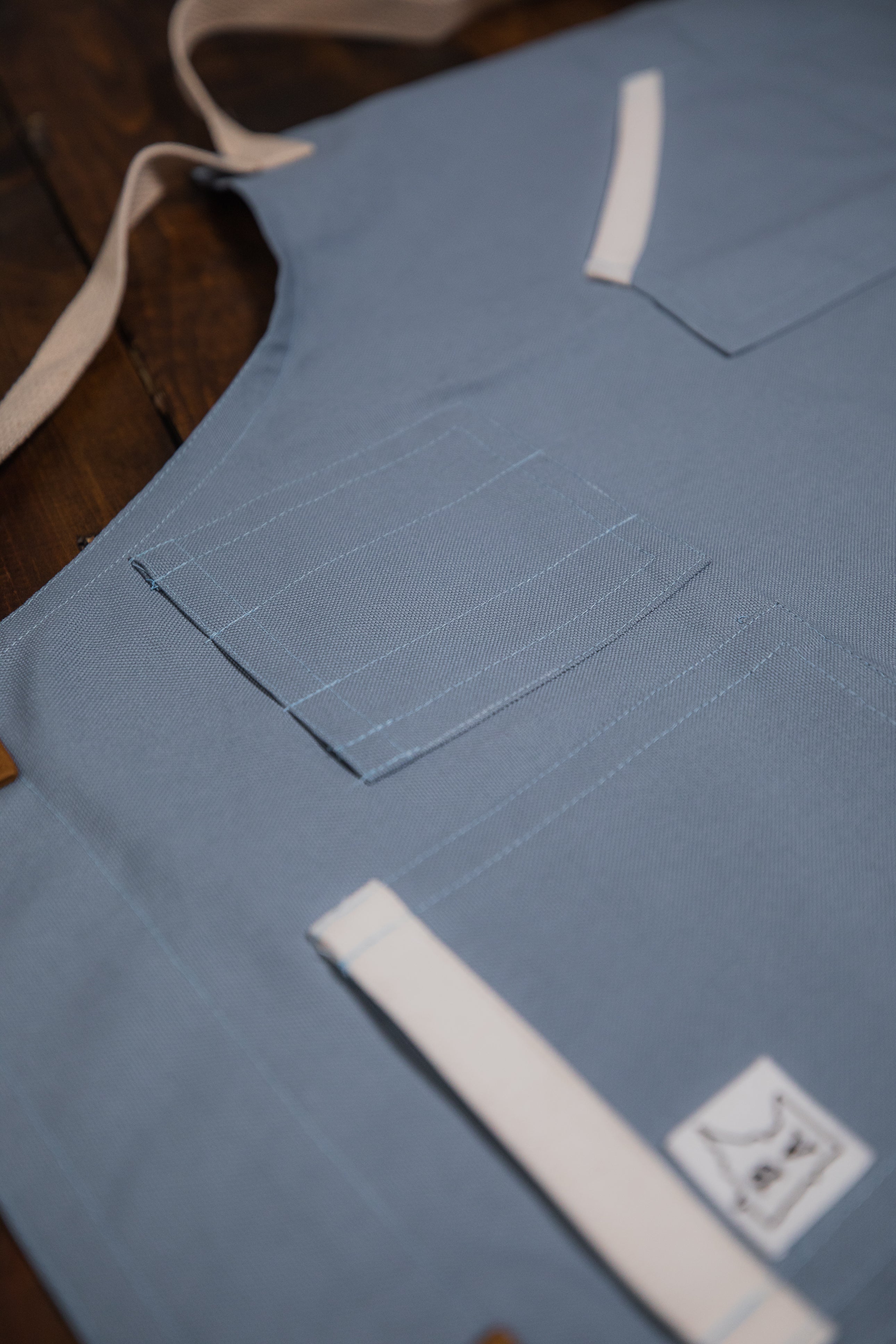 Product shot of Blue Opal cotton apron displaying the pen holder pockets on the left side of the chest. Produced by Craftmade Aprons, Minnesota.